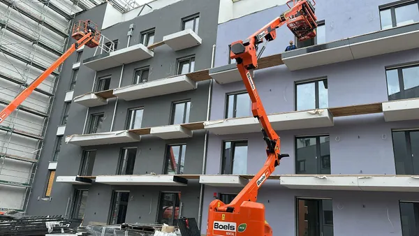 Zwei Hubarbeitsbühnen bei Montagearbeiten an einer mehrgeschossigen Wohnfassade.