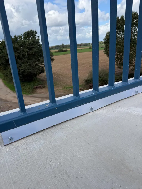 Blaue Geländerstäbe mit horizontaler Grundschiene und sichtbaren Befestigungen.